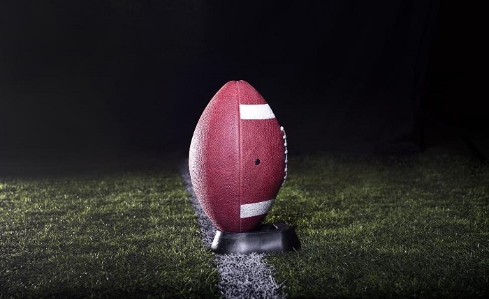 football resting in its stand on a grass football field with a black background